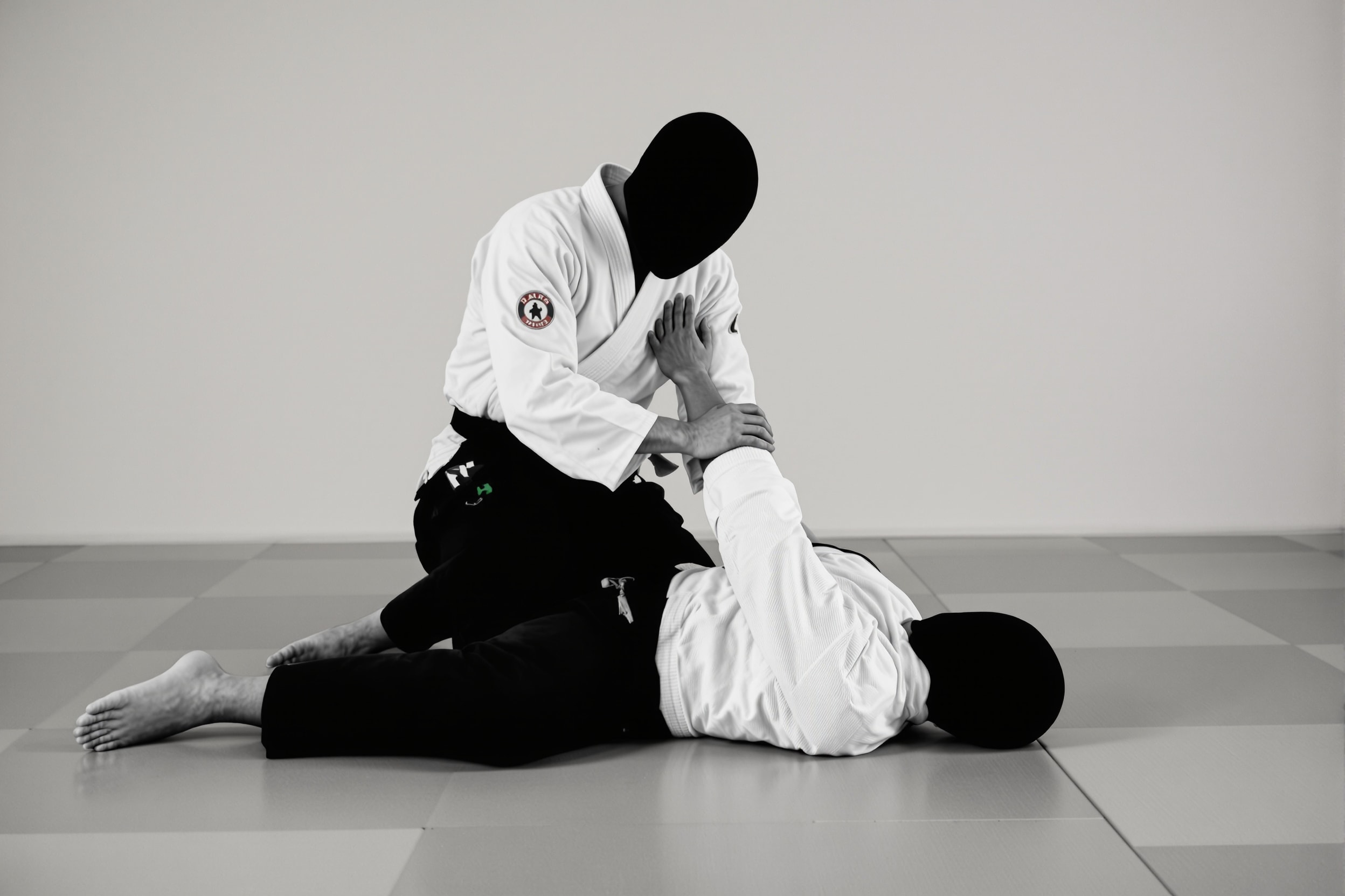 A kneeling aikido pin applied to a partner’s arm on the mat, faces obscured